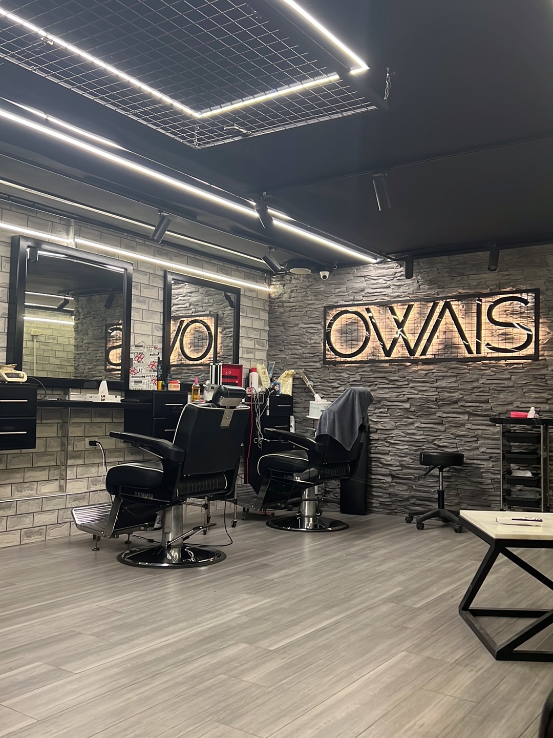 Salon Owais For Men interior with a wire-grid ceiling feature and the illuminated OWAIS sign on a stacked-stone wall