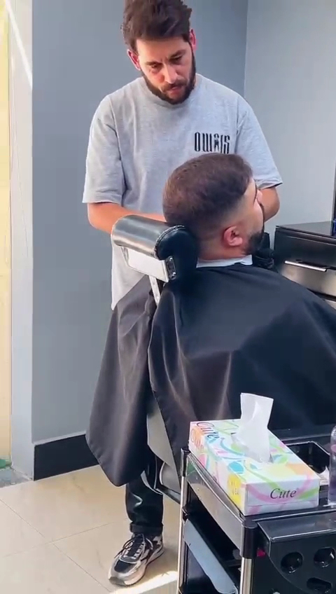 Barber in an Owais-branded shirt working on a client in a reclined barber chair