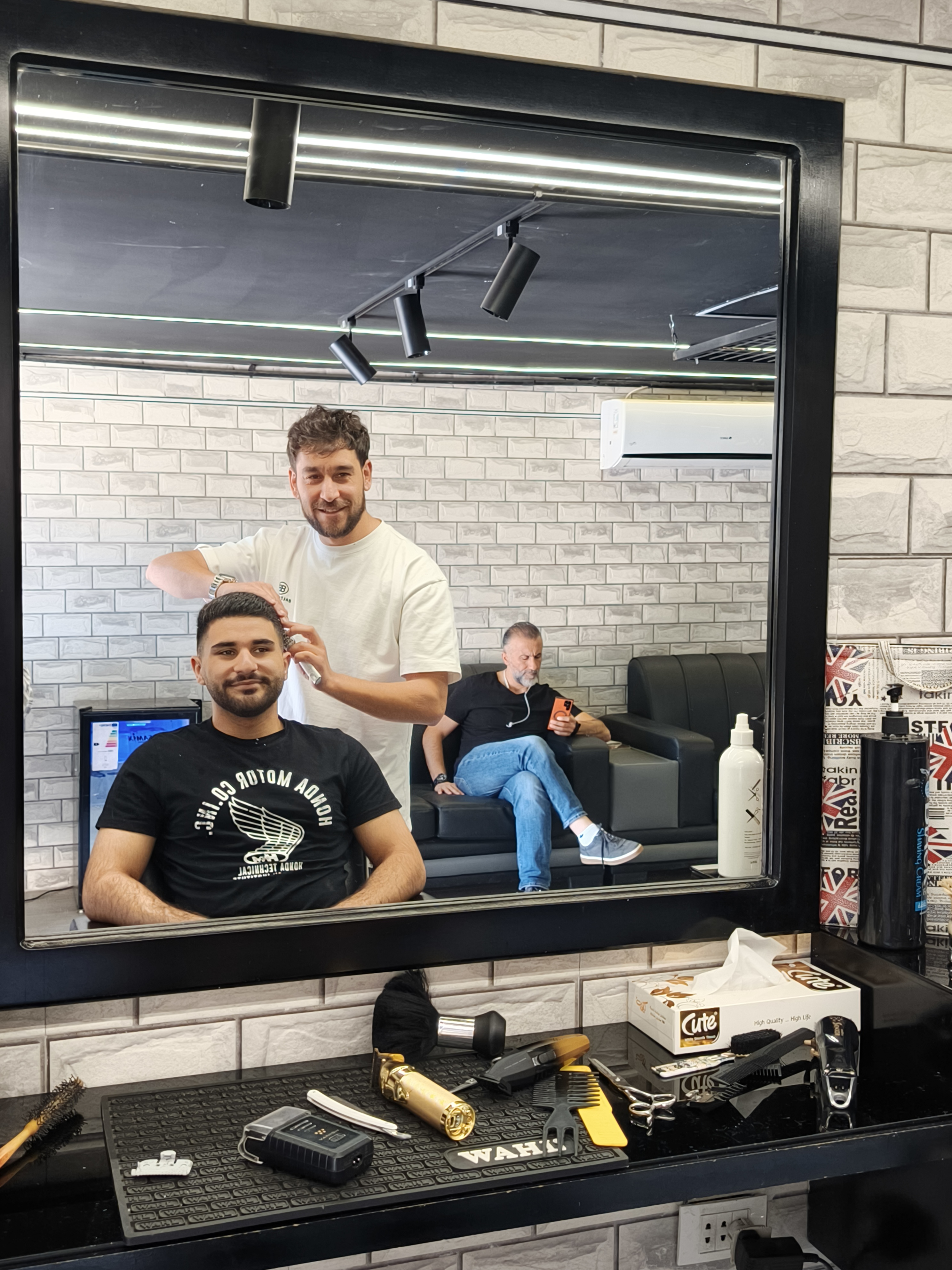 Barber finishing a cut with the waiting lounge visible in the mirror at Salon Owais
